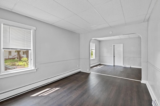 empty room featuring a drop ceiling, baseboard heating, and dark wood-type flooring