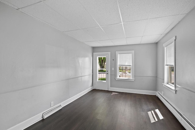 unfurnished room featuring baseboard heating, dark hardwood / wood-style floors, and a drop ceiling