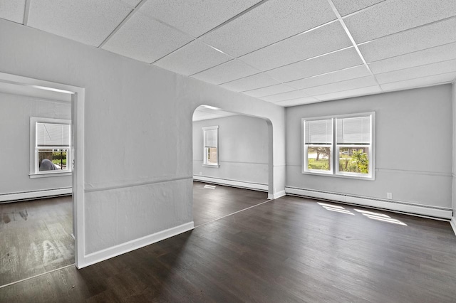 empty room with a baseboard heating unit, a paneled ceiling, and dark wood-type flooring