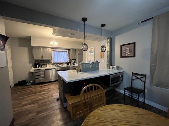 kitchen with dark hardwood / wood-style floors, kitchen peninsula, hanging light fixtures, gray cabinetry, and appliances with stainless steel finishes