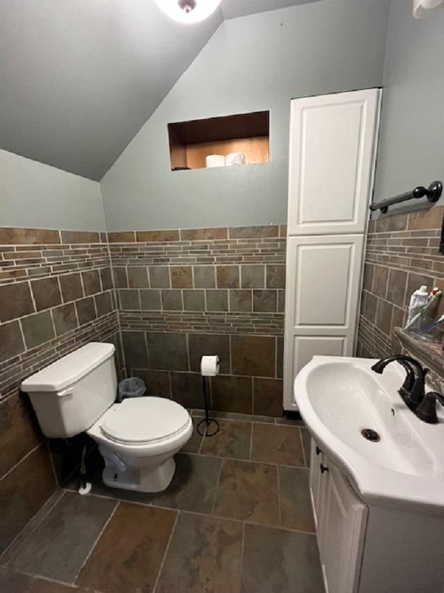 bathroom featuring vaulted ceiling, tile walls, toilet, tile flooring, and sink