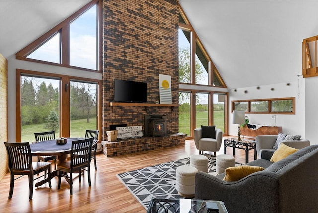 living room with high vaulted ceiling, a brick fireplace, a wood stove, and light hardwood / wood-style floors