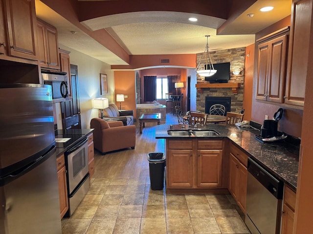 kitchen featuring kitchen peninsula, a stone fireplace, appliances with stainless steel finishes, sink, and a textured ceiling