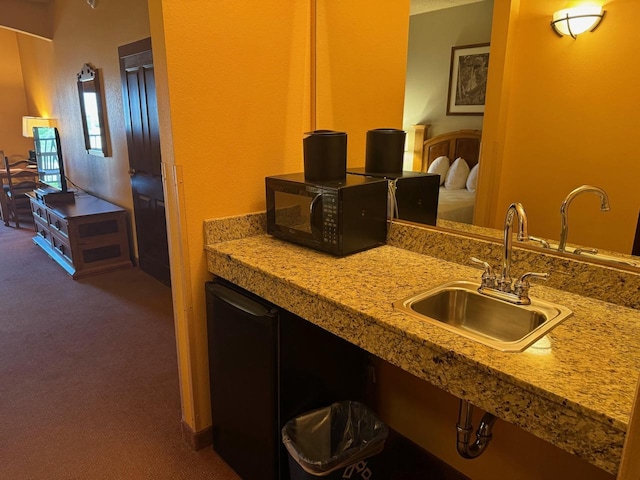 kitchen with dark colored carpet, light stone counters, and sink