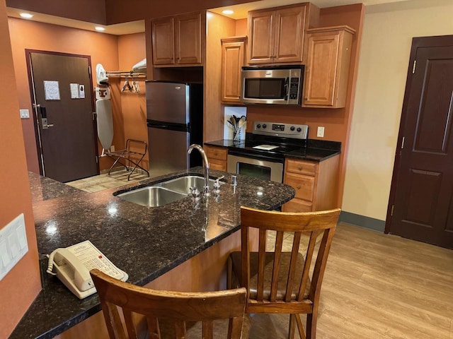 kitchen featuring dark stone counters, a kitchen breakfast bar, light wood-type flooring, sink, and appliances with stainless steel finishes