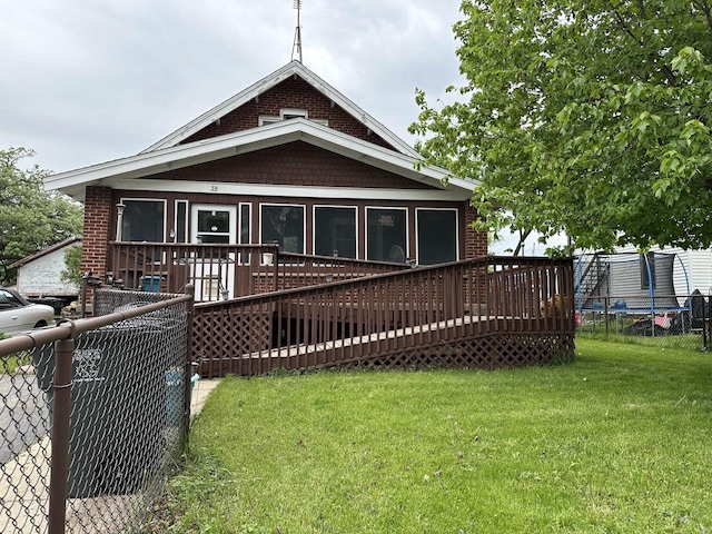 back of property featuring a trampoline, a wooden deck, and a yard