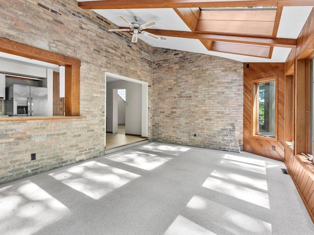 unfurnished living room featuring beam ceiling, wooden walls, high vaulted ceiling, and ceiling fan