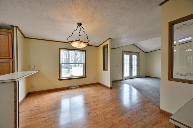 unfurnished dining area with plenty of natural light, vaulted ceiling, a textured ceiling, and light colored carpet