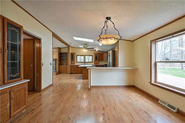 kitchen with light hardwood / wood-style floors, kitchen peninsula, vaulted ceiling with skylight, decorative light fixtures, and a textured ceiling