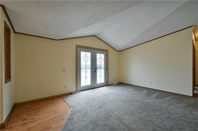 carpeted spare room with french doors, vaulted ceiling, and a textured ceiling