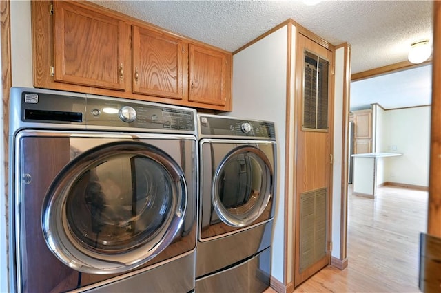 washroom featuring a textured ceiling, light hardwood / wood-style flooring, washing machine and clothes dryer, and cabinets