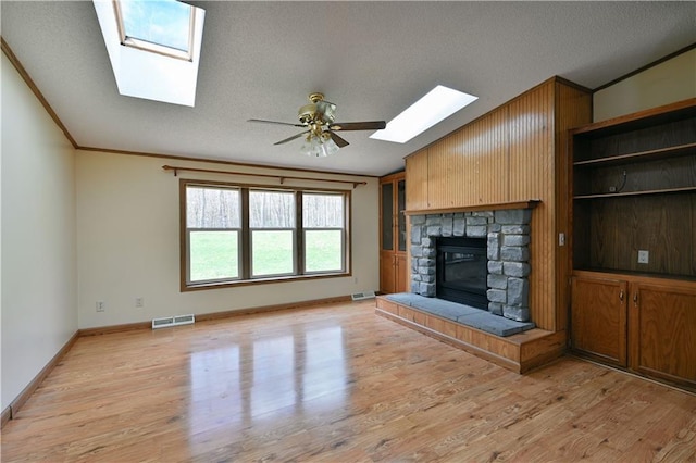 unfurnished living room with light hardwood / wood-style flooring, ceiling fan, crown molding, a stone fireplace, and wooden walls