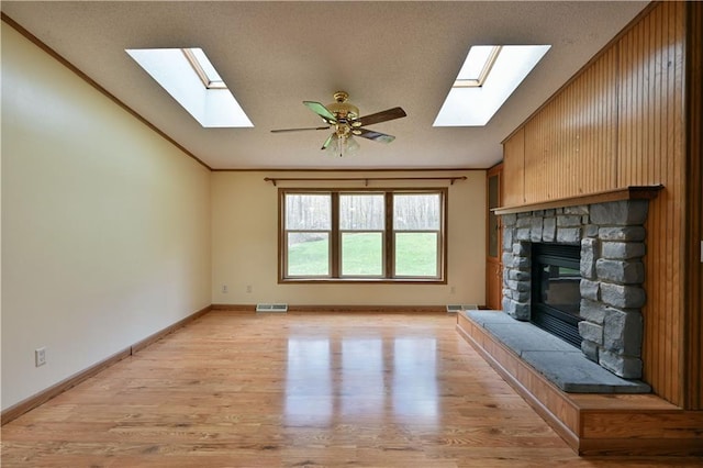 unfurnished living room featuring a stone fireplace, ceiling fan, light hardwood / wood-style floors, a textured ceiling, and ornamental molding