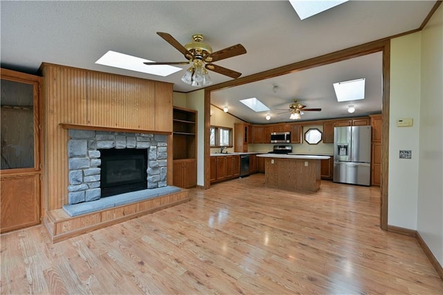 kitchen featuring a fireplace, a kitchen island, stainless steel appliances, ceiling fan, and light wood-type flooring