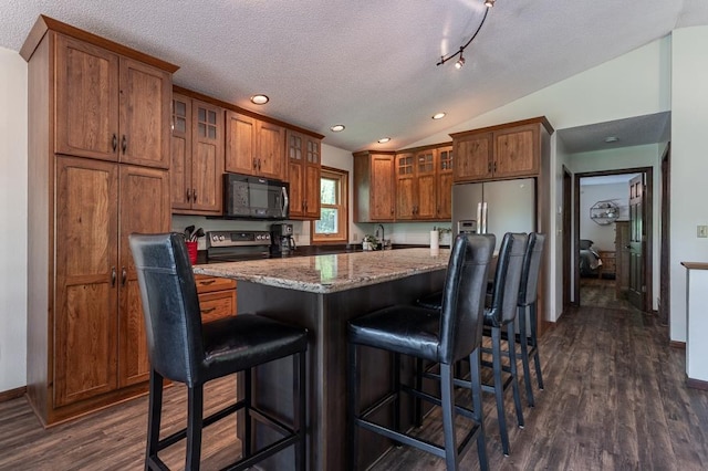 kitchen featuring lofted ceiling, a kitchen bar, a kitchen island, stainless steel appliances, and light stone countertops