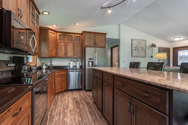 kitchen with appliances with stainless steel finishes, lofted ceiling, dark stone counters, dark wood-type flooring, and a textured ceiling