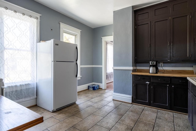 kitchen featuring white fridge, light tile flooring, and dark brown cabinets