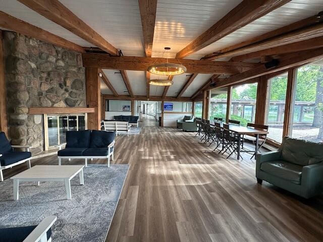 living room with a stone fireplace, lofted ceiling with beams, and wood-type flooring