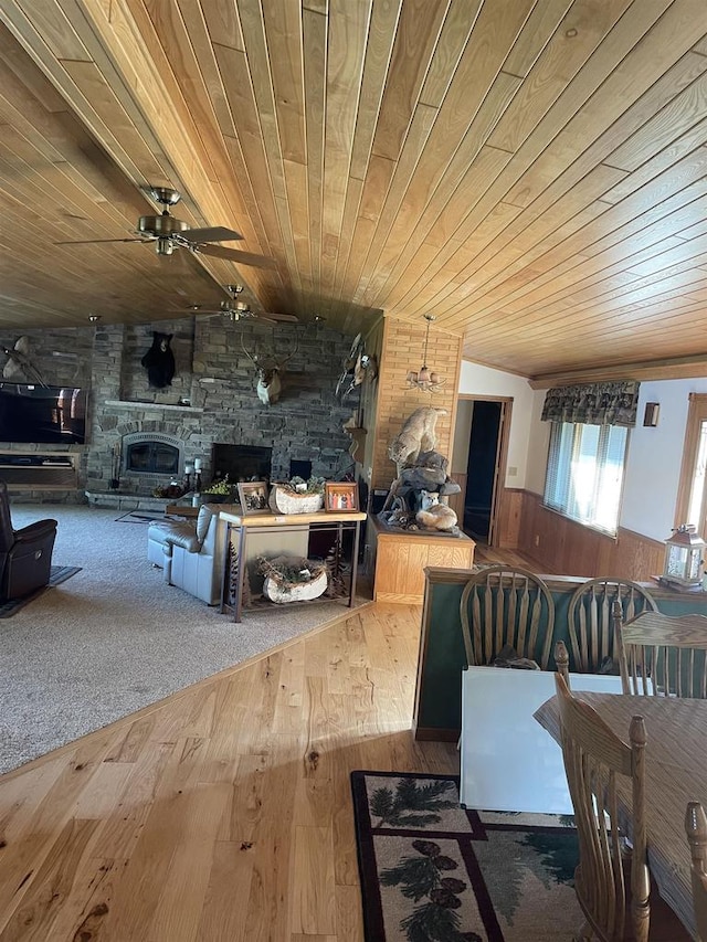 dining room featuring ceiling fan, a stone fireplace, wood-type flooring, and wood ceiling