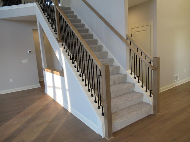 staircase with a towering ceiling and hardwood / wood-style floors