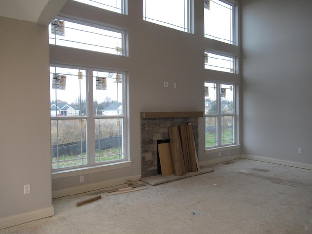 unfurnished living room featuring a stone fireplace, a wealth of natural light, and a high ceiling