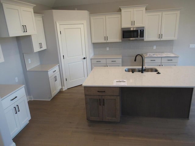 kitchen with dark wood-type flooring, sink, white cabinetry, an island with sink, and decorative backsplash