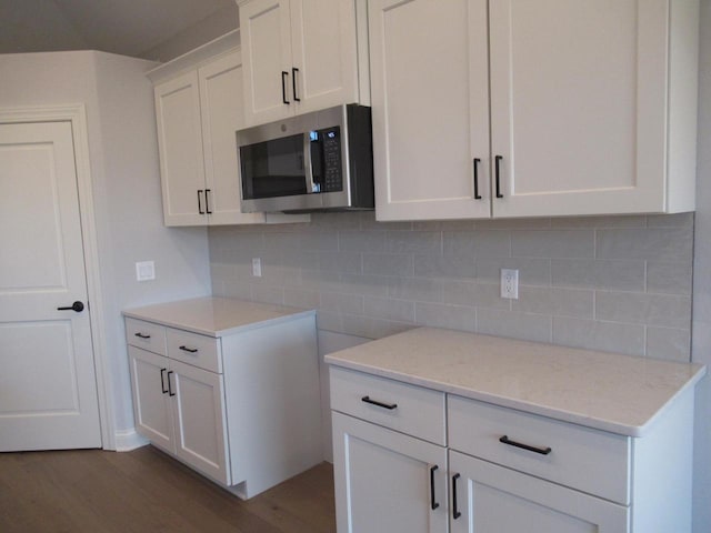 kitchen featuring light stone counters, backsplash, dark wood-type flooring, and white cabinets