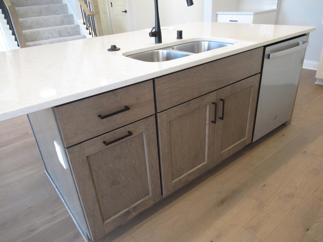 kitchen with a kitchen island with sink, sink, light hardwood / wood-style flooring, and stainless steel dishwasher