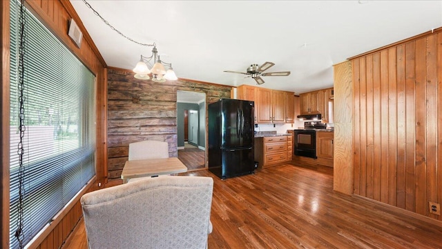 kitchen with black appliances, ceiling fan with notable chandelier, wood walls, and dark hardwood / wood-style flooring