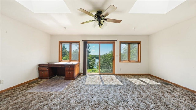 empty room featuring a skylight, ceiling fan, plenty of natural light, and carpet floors