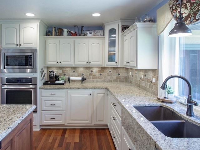 kitchen featuring appliances with stainless steel finishes, light stone counters, sink, pendant lighting, and white cabinets