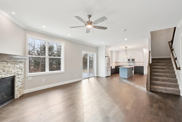 unfurnished living room featuring stairs, ornamental molding, a fireplace, and dark wood finished floors