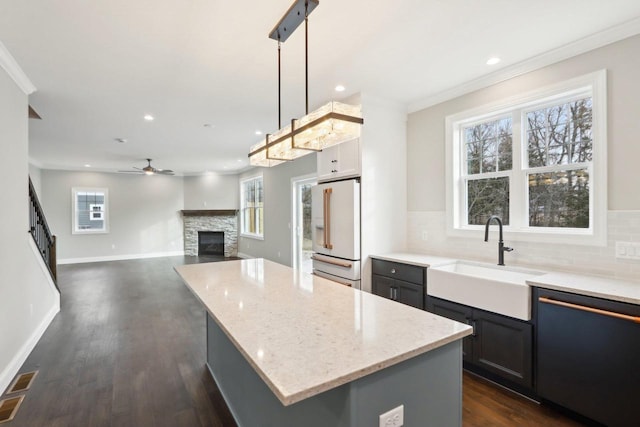 kitchen featuring light stone counters, a stone fireplace, a sink, high end fridge, and dishwasher