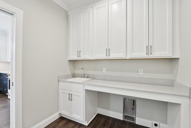 laundry room featuring dark wood-style flooring, cabinet space, a sink, and baseboards