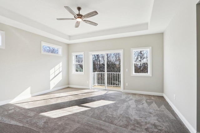 carpeted spare room featuring a tray ceiling, ceiling fan, and baseboards