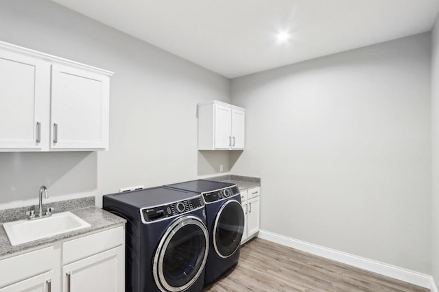 clothes washing area featuring light wood finished floors, cabinet space, washing machine and dryer, a sink, and baseboards