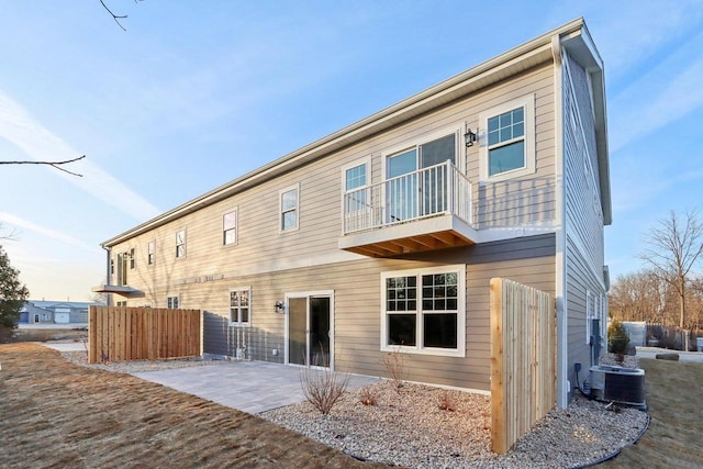 rear view of property featuring central AC unit, a patio area, fence, and a balcony