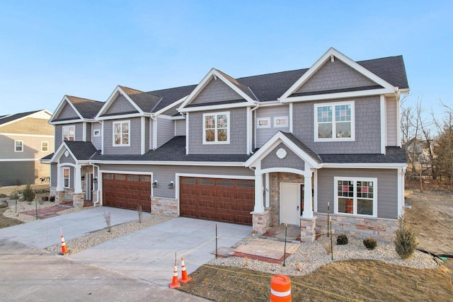 view of front of property with stone siding, roof with shingles, and concrete driveway