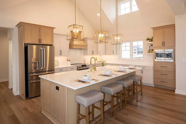 kitchen featuring appliances with stainless steel finishes, dark hardwood / wood-style flooring, light brown cabinetry, a kitchen island with sink, and high vaulted ceiling