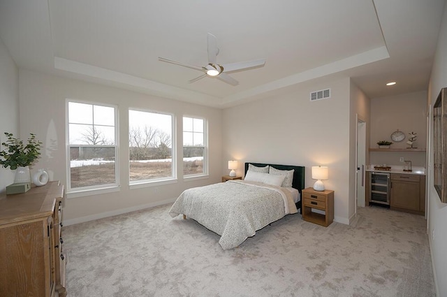 carpeted bedroom with a tray ceiling, beverage cooler, and ceiling fan