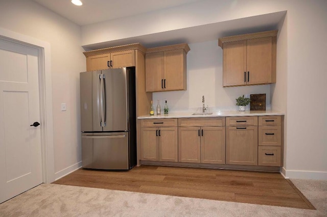 kitchen featuring light brown cabinets, light wood-type flooring, sink, and stainless steel refrigerator