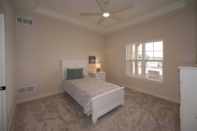 bedroom with light carpet, a tray ceiling, and ceiling fan