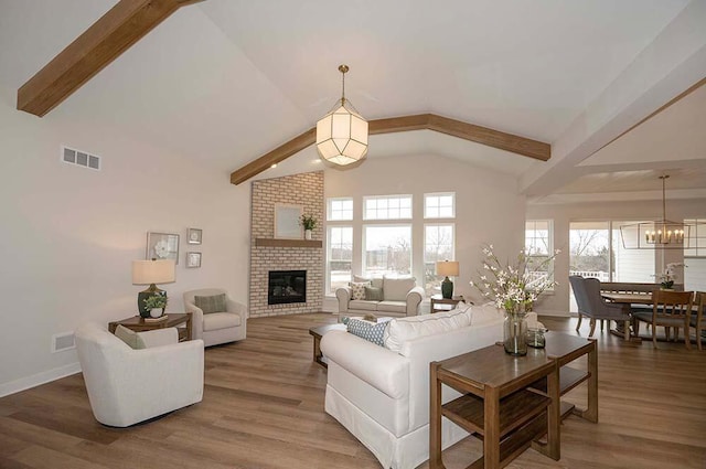 living room featuring a fireplace, vaulted ceiling with beams, hardwood / wood-style flooring, and an inviting chandelier