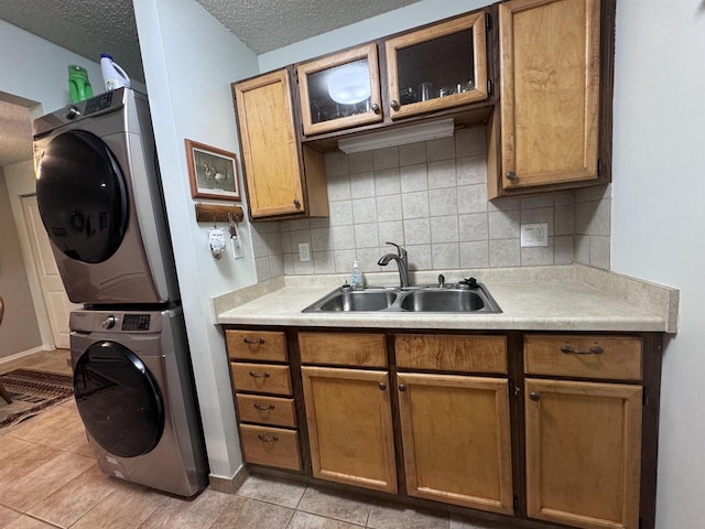 kitchen featuring sink, stacked washing maching and dryer, backsplash, a textured ceiling, and light tile patterned floors