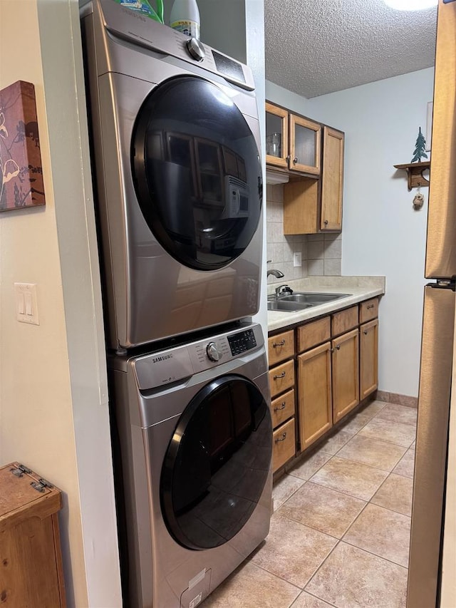 clothes washing area featuring stacked washer / drying machine, sink, light tile patterned floors, and a textured ceiling