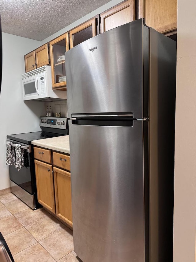 kitchen with light tile patterned floors, a textured ceiling, appliances with stainless steel finishes, and tasteful backsplash