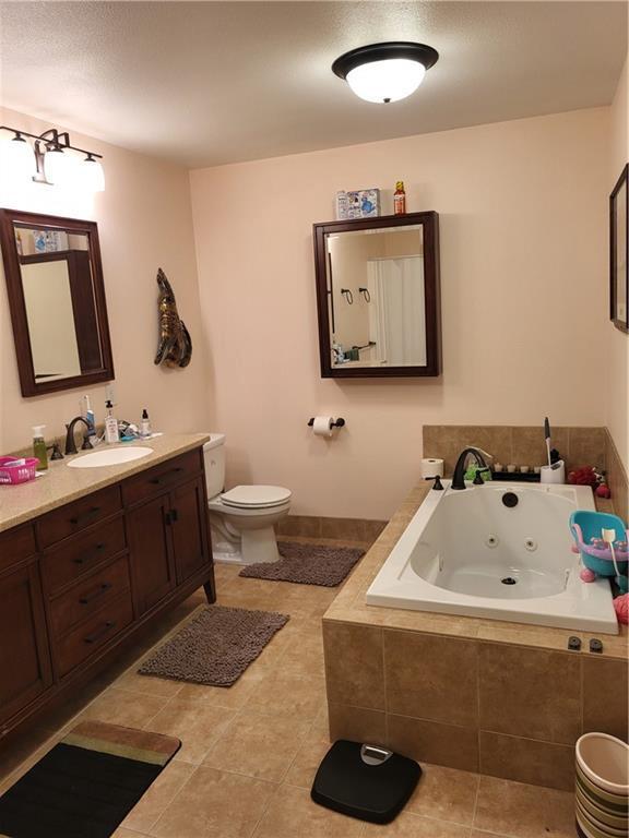 bathroom featuring tile patterned floors, vanity, a relaxing tiled tub, and toilet