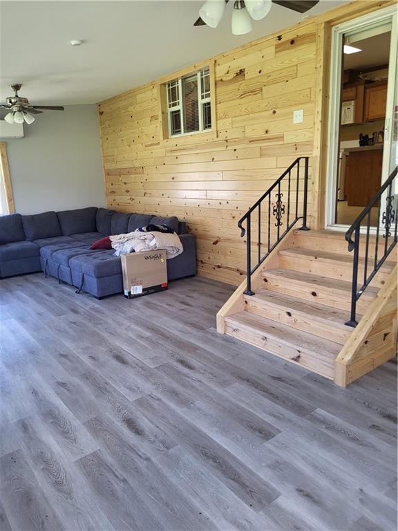 unfurnished living room with wooden walls, ceiling fan, and wood-type flooring