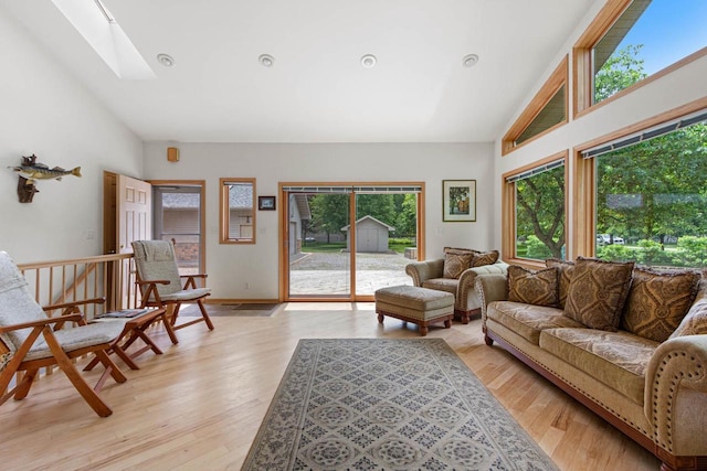 living room featuring light hardwood / wood-style floors, high vaulted ceiling, and a skylight