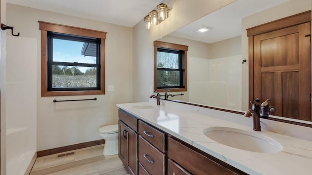 full bath featuring double vanity, a sink, toilet, and baseboards